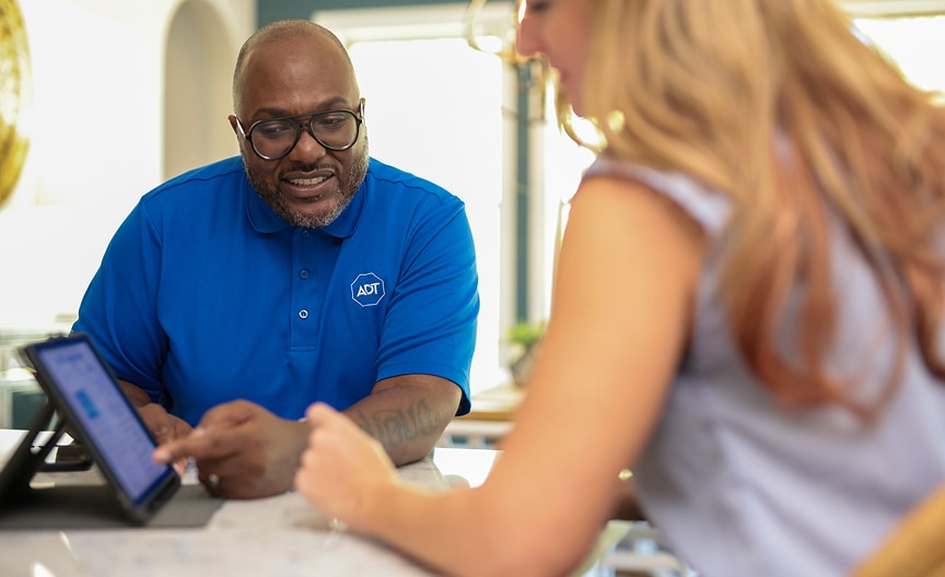 Woman self installing an ADT indoor camera on a shelf in her home Woman self installing an ADT indoor camera on a shelf in her home